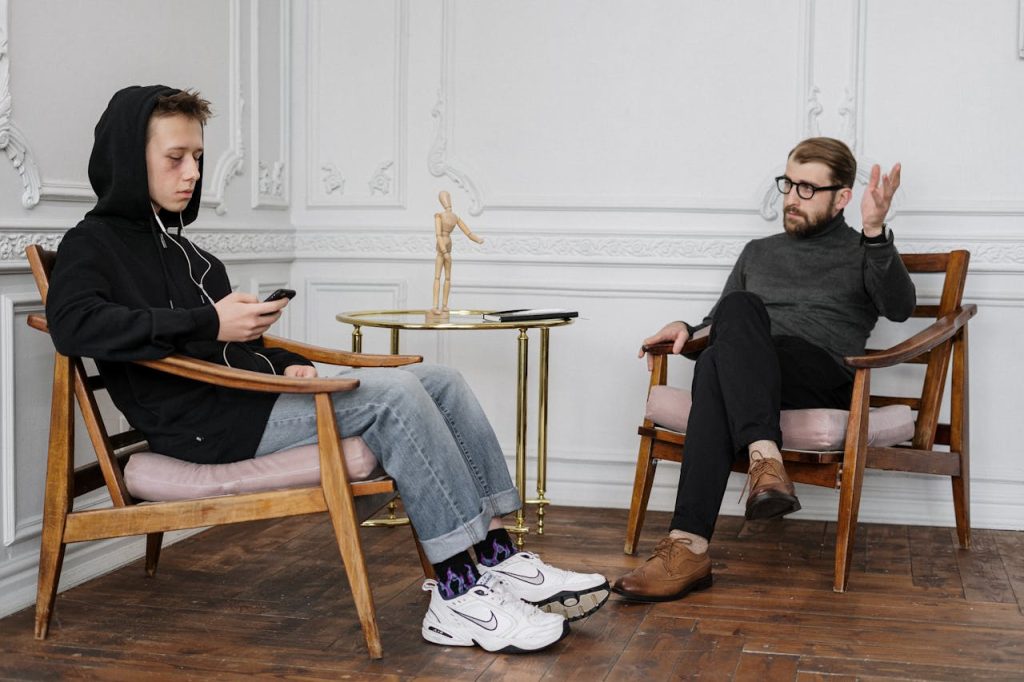 Teenage boy in hoodie during a therapy session with a male therapist.